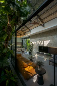 A modern living room featuring glass walls, stone accents, and concrete floors, with a comfortable seating area and a flat-sc