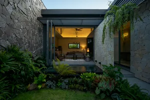 A modern living space with concrete walls and a glass wall, featuring a cozy seating area and a small indoor pool with surrou