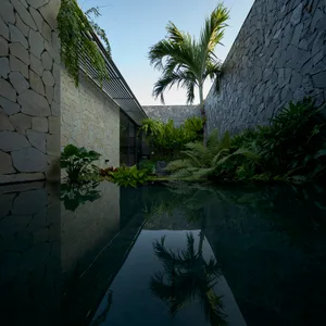Modern outdoor pool with stone walls and lush greenery surrounding it.