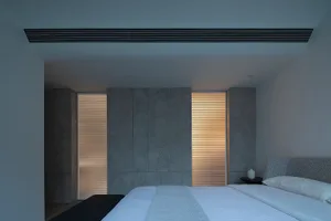 Spacious minimalist bedroom featuring concrete walls, wooden floor, and simple furniture.
