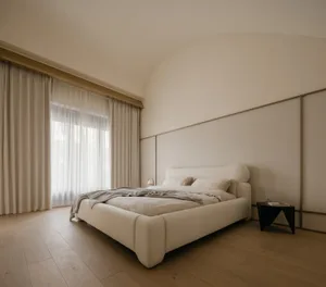 A minimalist bedroom with a neutral-toned bed featuring soft textiles and a modern side table.