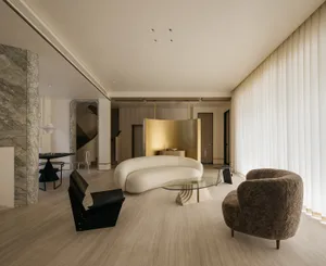 A modern residential interior with minimalist design elements, featuring a circular sofa, abstract armchair, and glass coffee
