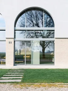 A large, double-height glass window with an arched top in a minimalistic architectural setting.