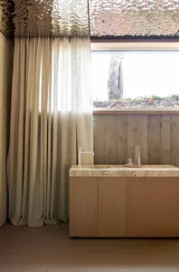 Modern minimalist bathroom featuring marble countertop and wood cabinetry, with gray curtains and natural light.