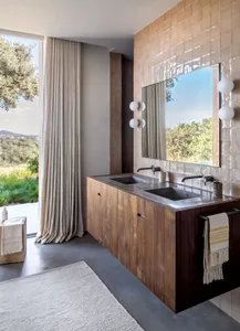 A minimalist bathroom features a wood vanity, tiled walls, and a large mirror reflecting a natural view.