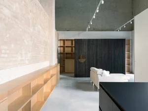 A minimalist living room with concrete floors, wooden shelves, and metal accents, featuring a white sofa and a dark wooden wa