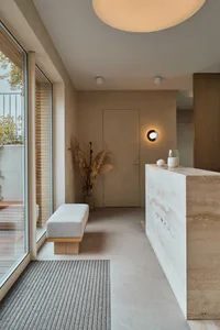 Modern minimalist lobby featuring a concrete floor, wooden bench, and glass lighting fixture.