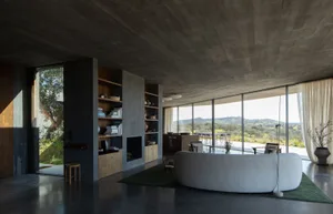 Modern living room with concrete walls, floor, and ceiling, featuring a large circular sofa and a bookshelf filled with books