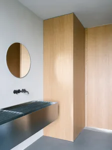 Modern minimalist bathroom with wooden walls and a circular mirror.