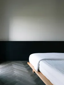 A modern minimalist bedroom featuring a wood platform bed with white bedding against a black and white color block wall.