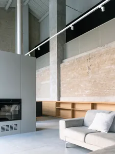 A modern minimalist living room with concrete walls, a white couch, and a gray fireplace.