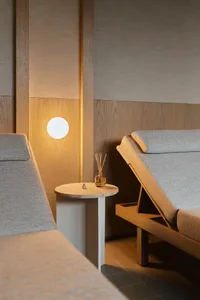 A minimalist spa room with wooden walls, fabric seating, and a small side table with a diffuser.