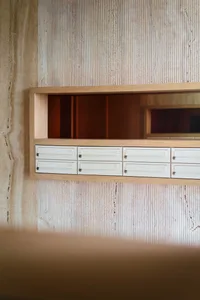 A white mailbox setup with wooden shelves on a textured concrete wall