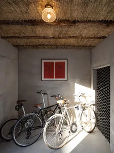 Bicycles parked in a minimalist bicycle garage with a thatched roof and concrete flooring.