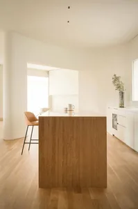 A minimalist kitchen with white cabinets, wooden flooring, and a large island.
