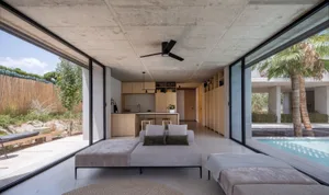 Spacious, minimalist living room featuring a concrete floor and large windows, with a contemporary sectional sofa and a view 