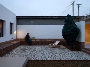 A modern exterior residential space featuring a rendered concrete patio and seating area with a person sitting on a bench.