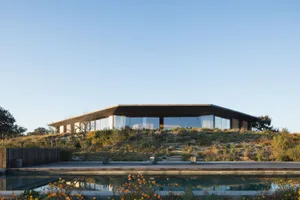 A modern house with large glass windows surrounded by greenery and a wooden deck.