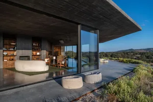 A contemporary living room with a concrete ceiling and floor, featuring minimalist furniture and large windows overlooking th