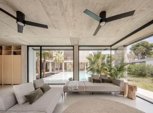 A modern living room featuring a sleek concrete ceiling and walls, with large windows offering a view of a pool and tropical 