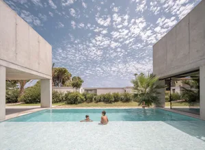 Two children swimming in a modern pool surrounded by concrete tiles and tropical vegetation.