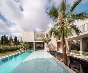 A modern residential house with concrete and glass exterior materials, featuring a pool and palm trees.