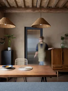 A rustic dining room featuring a wooden table with woven placemats, a concrete floor, and wicker pendant lights hanging above