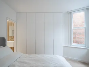 A minimalist bedroom with a white bed and a large white wardrobe.