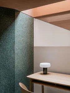 A minimalist office space featuring a desk made of wood with a modern, round lamp and a wall with a combination of terrazzo a