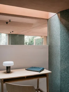 A modern home office featuring a sleek desk, a minimalist lamp, and a leather notebook against a concrete backdrop.