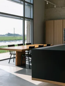 Modern dining room with wooden furniture and large windows overlooking green fields.