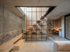 Modern living room and office space featuring concrete, black metal, and wood elements.