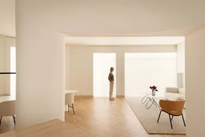 A modern minimalist lounge area with neutral tones, featuring a white sofa, wooden floor, and large windows.