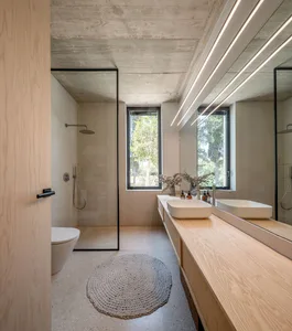 A modern minimalist bathroom with a white concrete floor, walls, and ceiling. The room features two white sinks with wooden c
