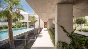 A modern residential exterior made of concrete with a patio area featuring a pool and palm trees.