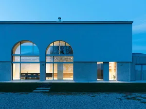 Modern residential building with white plaster walls and large arched windows.