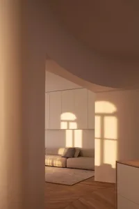 A minimalist living room with natural light streaming in through the windows, featuring a grey L-shaped sofa and taupe floori