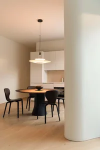 Modern minimalist dining area with a round wooden table and black chairs.