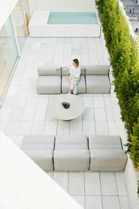 A modern minimalist patio space with clean lines, light grey furniture, and a small pool surrounded by greenery.