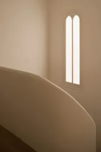 A modern staircase with a unique wall and a narrow, high window.