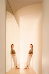 A person standing in a minimalist corridor with neutral tones.