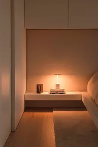 A minimalist bedroom with white furnishings, wood flooring, and overhead lighting.