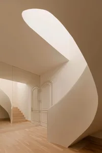 A modern, white, space with curved, white walls and a spiral staircase.