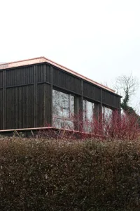 A modern building with black cladding and a copper roof, viewed from the side.