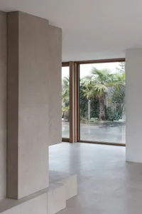 Modern minimalist interior with concrete columns and large windows overlooking a tropical garden.