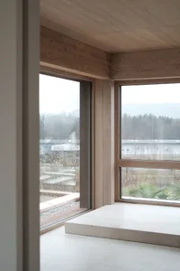 Minimalist architectural space with large windows featuring wooden frames and flooring.