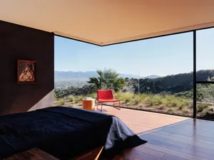 Minimalist bedroom with a wooden floor, large glass window, and red chair.
