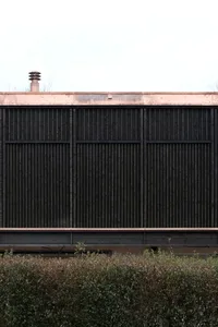 A modern arbor with a dark wooden slat design and a copper roof.