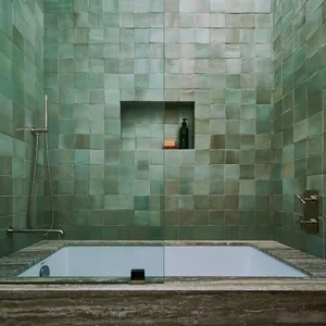 A modern bathroom featuring green square tiles on the walls, a built-in bathtub, and a shower area.