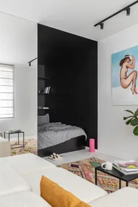Modern bedroom with black concrete walls, white furniture, and colorful rug.
